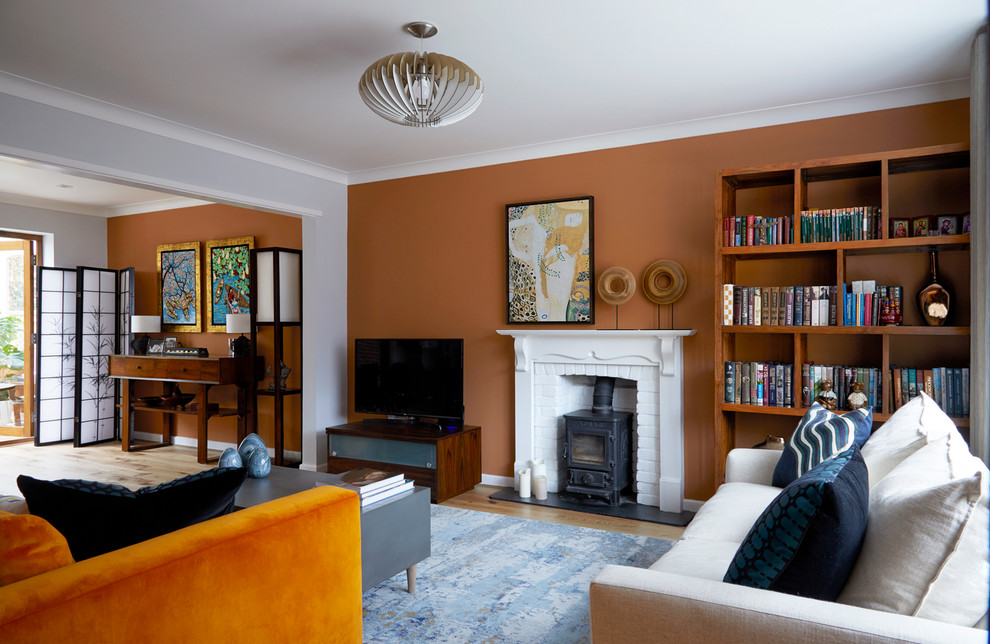 На фото: гостиная комната среднего размера в стиле неоклассика (современная классика) с оранжевыми стенами, печью-буржуйкой, фасадом камина из штукатурки, отдельно стоящим телевизором и коричневым полом