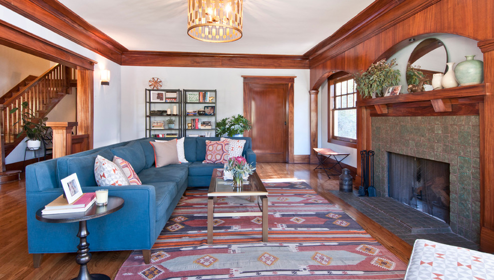 Идея дизайна: гостиная комната в стиле кантри с паркетным полом среднего тона, стандартным камином, фасадом камина из плитки и синим диваном