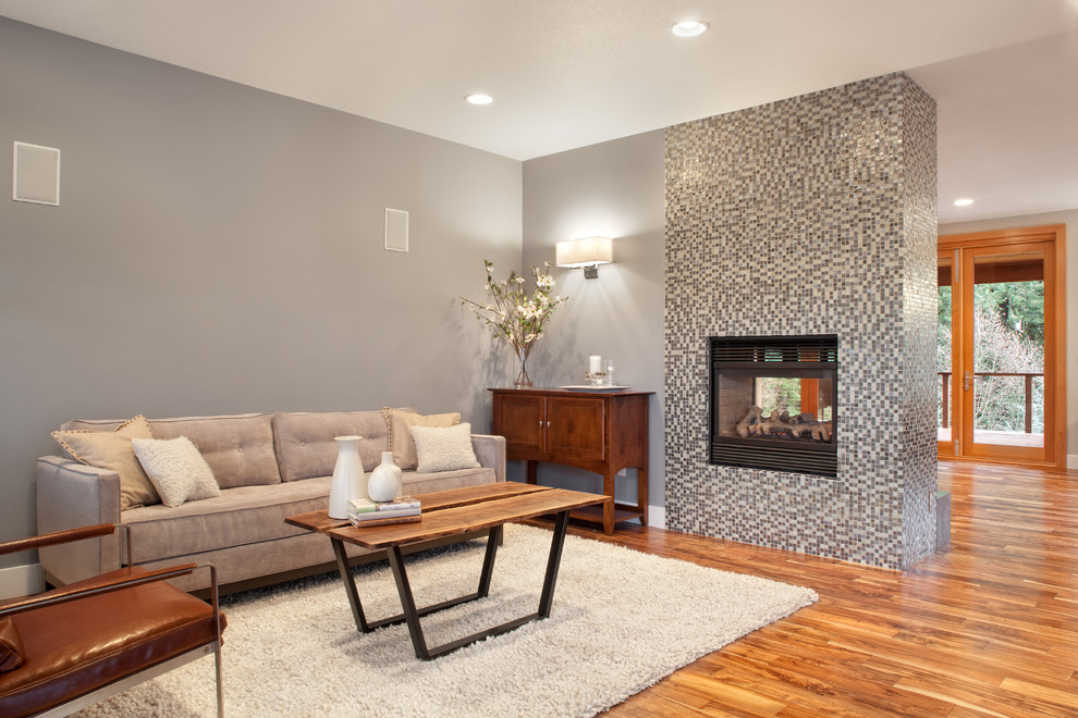 Cette image montre un salon minimaliste ouvert avec un mur bleu, un sol en bois brun, une cheminée double-face et un manteau de cheminée en carrelage.