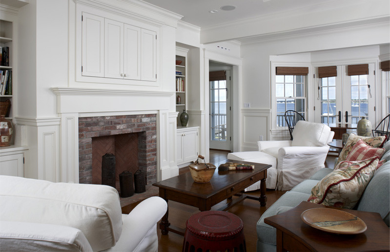Cette image montre un salon marin de taille moyenne et ouvert avec un mur blanc, un sol en bois brun, une cheminée standard, un manteau de cheminée en brique et un téléviseur dissimulé.