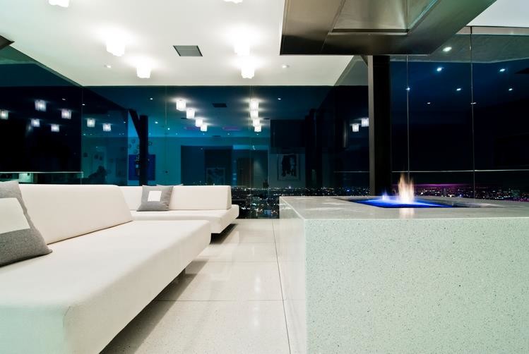 Идея дизайна: огромная парадная, двухуровневая гостиная комната в стиле модернизм с полом из керамогранита, двусторонним камином, фасадом камина из камня, белым полом и многоуровневым потолком