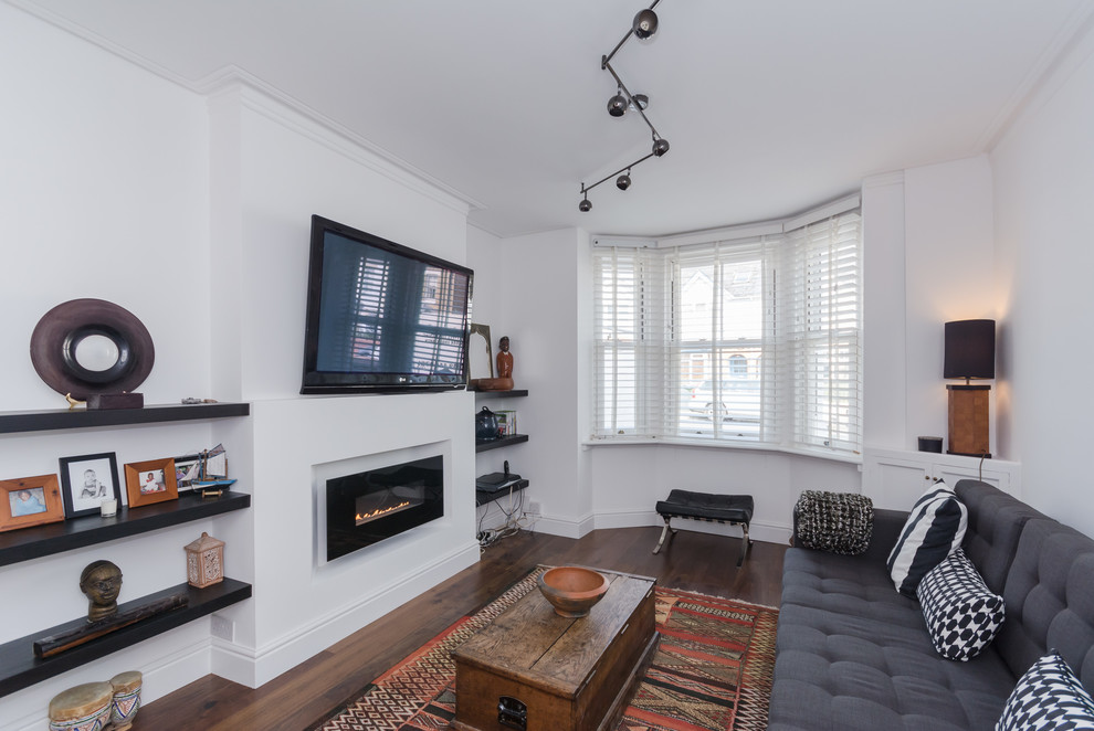 Modern inredning av ett mellanstort separat vardagsrum, med vita väggar, mörkt trägolv, en bred öppen spis, en spiselkrans i gips, en väggmonterad TV och brunt golv