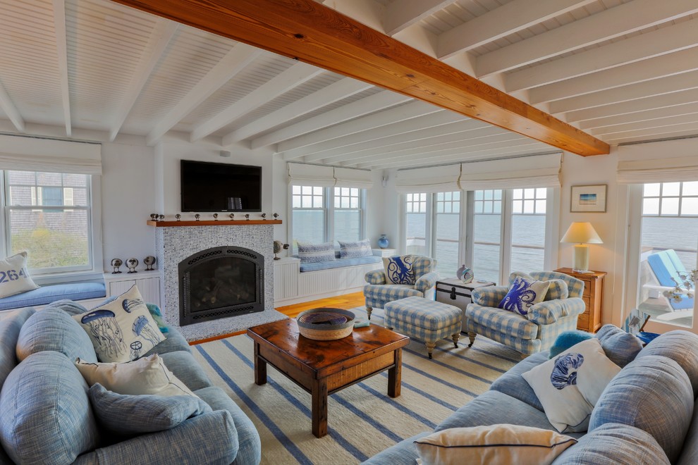 Photo of a beach style living room in Boston with white walls, medium hardwood flooring, a standard fireplace, a tiled fireplace surround and a wall mounted tv.