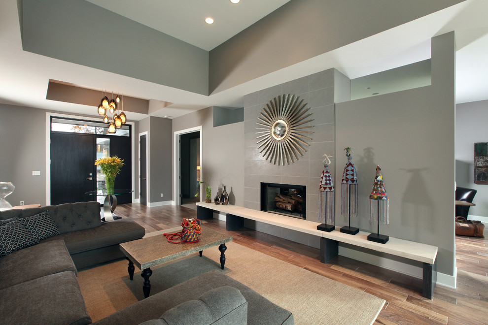 Cette image montre un grand salon design ouvert avec un mur gris, un sol en bois brun, une cheminée standard et un manteau de cheminée en pierre.