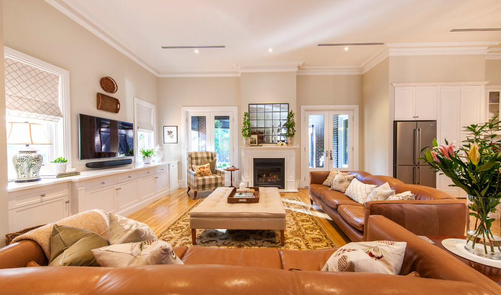 На фото: открытая гостиная комната в классическом стиле с бежевыми стенами, паркетным полом среднего тона, стандартным камином, телевизором на стене, желтым полом и коричневым диваном с