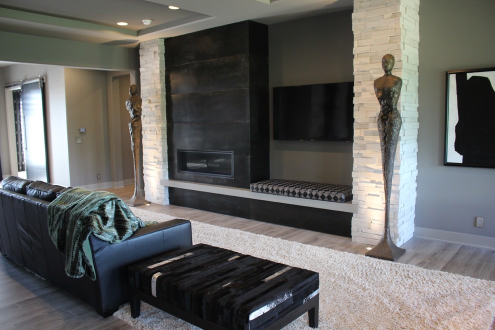 Modelo de salón abierto minimalista con paredes grises, chimenea lineal, marco de chimenea de piedra y televisor colgado en la pared