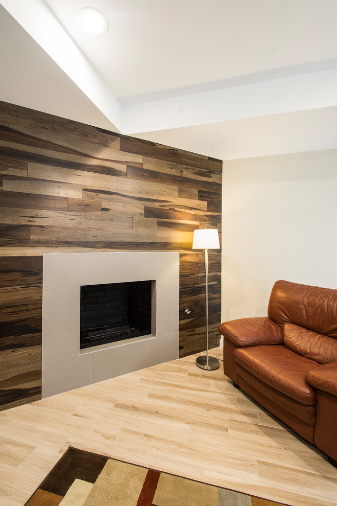 Modelo de salón abierto de estilo americano grande con paredes beige, suelo de madera clara, marco de chimenea de piedra, suelo beige, todas las chimeneas y televisor colgado en la pared
