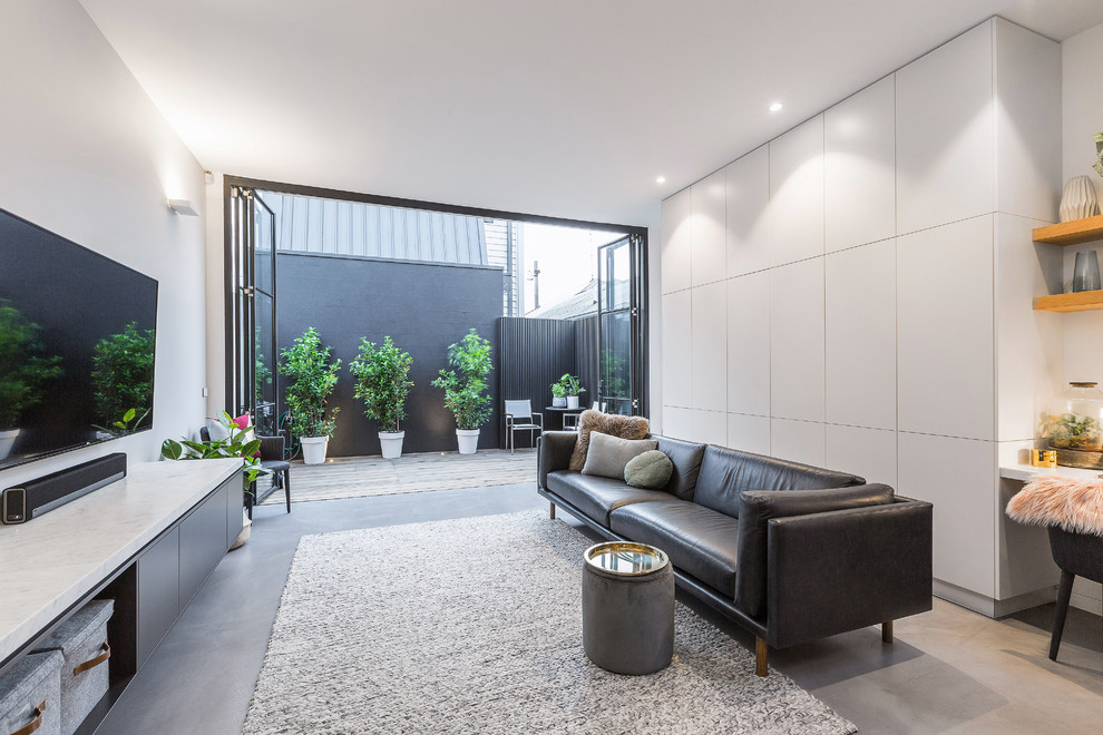Cette image montre un salon design de taille moyenne et ouvert avec un mur gris, sol en béton ciré, un téléviseur fixé au mur et un sol gris.