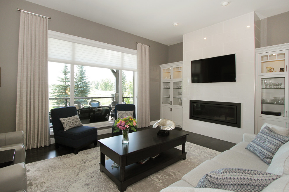 Großes, Offenes Klassisches Wohnzimmer mit grauer Wandfarbe, dunklem Holzboden, Hängekamin, gefliester Kaminumrandung, Multimediawand und schwarzem Boden in Calgary