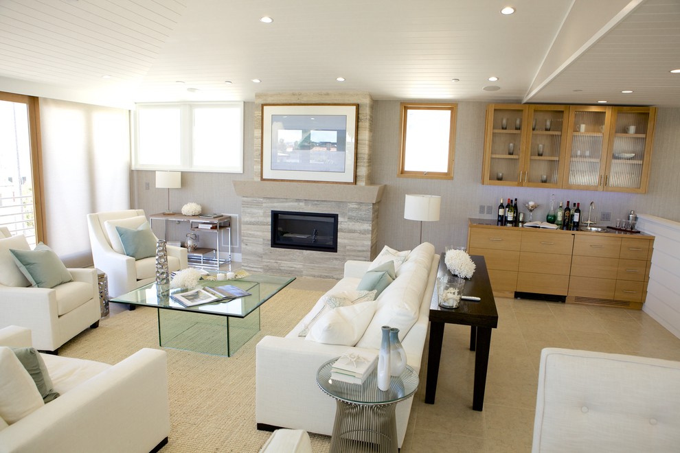 Источник вдохновения для домашнего уюта: большая открытая гостиная комната в морском стиле с домашним баром, белыми стенами, полом из известняка, стандартным камином и фасадом камина из камня