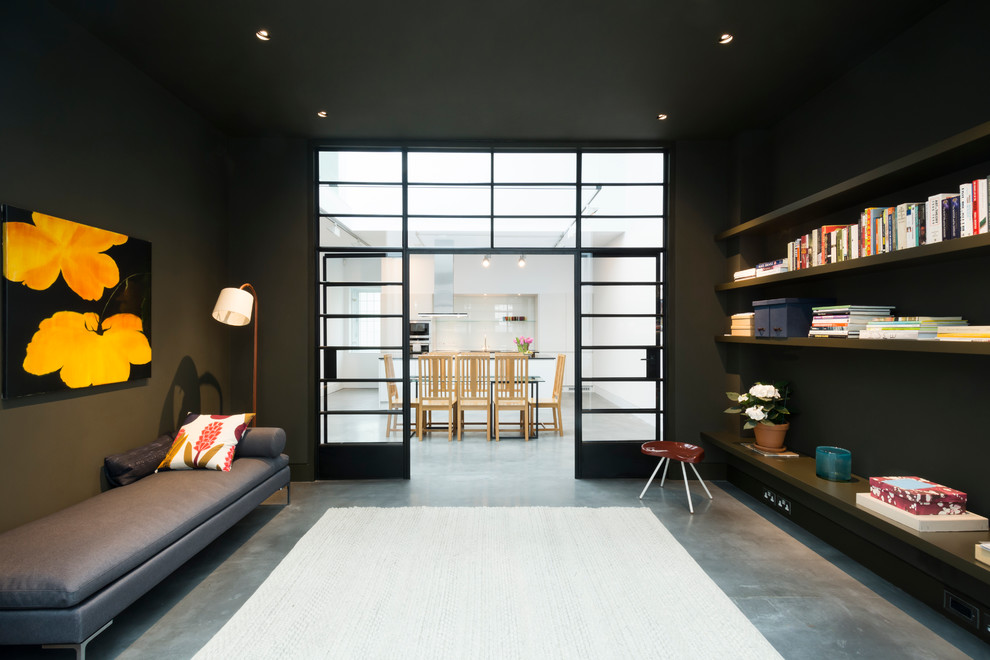Idee per un ampio soggiorno industriale aperto con pareti nere, libreria e pavimento in cemento