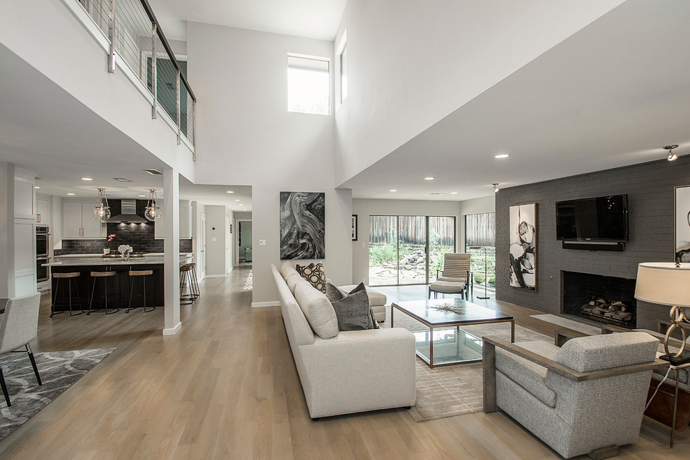 Стильный дизайн: большая открытая гостиная комната в стиле модернизм с серыми стенами, светлым паркетным полом, стандартным камином, фасадом камина из кирпича и телевизором на стене - последний тренд