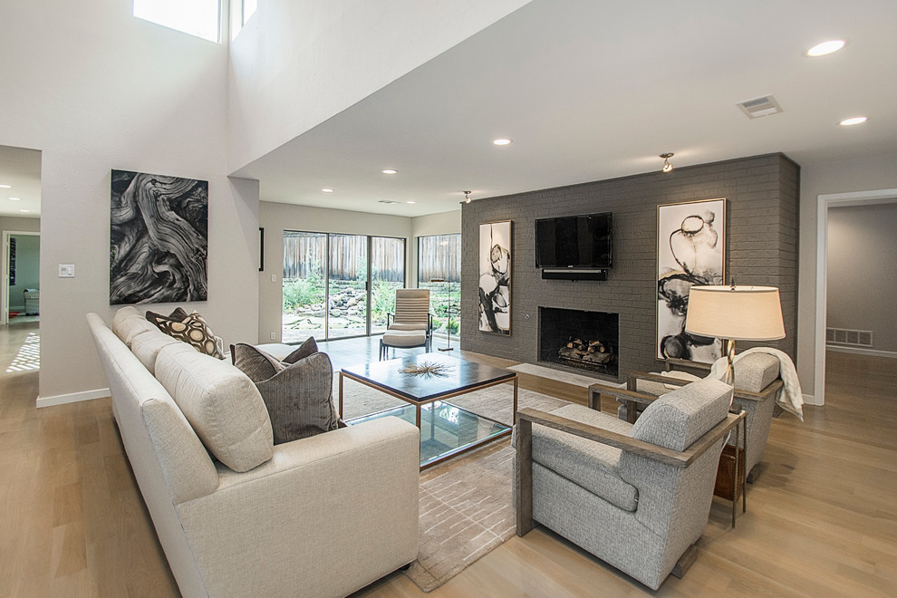 This is an example of a modern open plan living room in Dallas with grey walls, light hardwood flooring, a standard fireplace, a brick fireplace surround and a wall mounted tv.