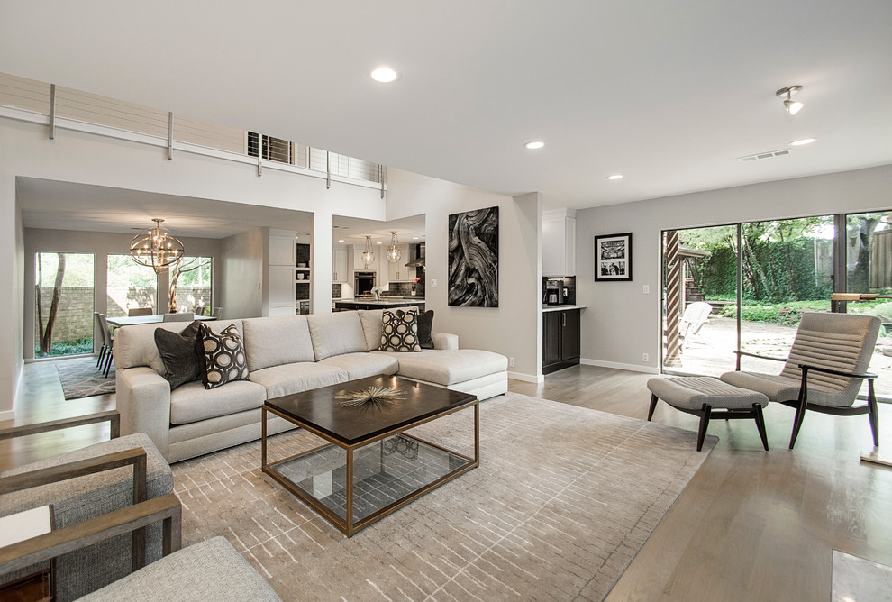 Modern open plan living room in Dallas with grey walls, light hardwood flooring, a standard fireplace, a brick fireplace surround, a wall mounted tv and feature lighting.