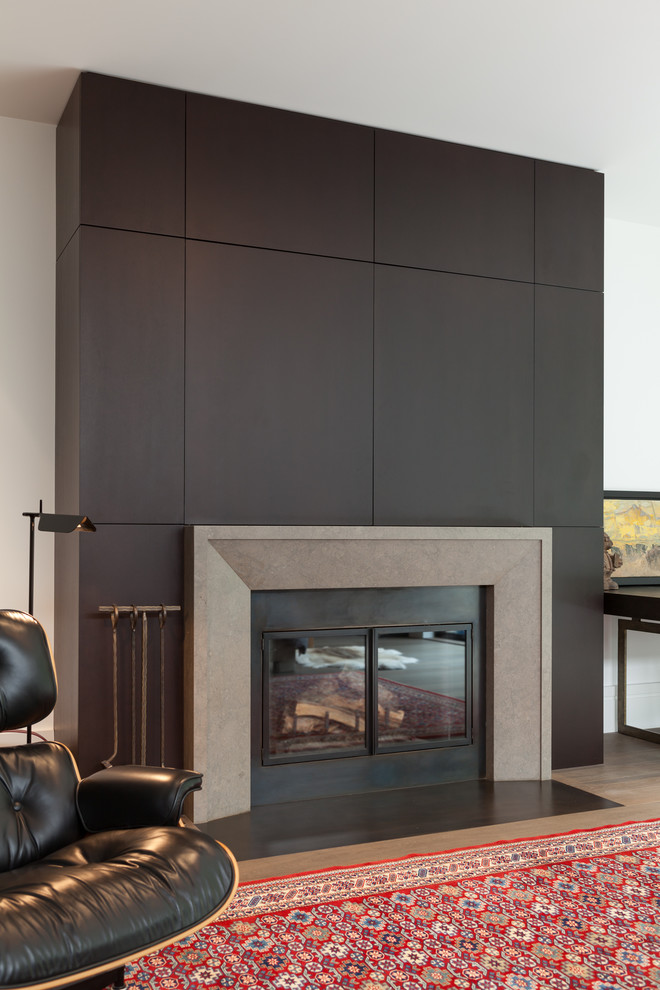 Example of a mid-sized minimalist enclosed light wood floor and brown floor living room design in San Francisco with a standard fireplace, a wood fireplace surround, a concealed tv and white walls