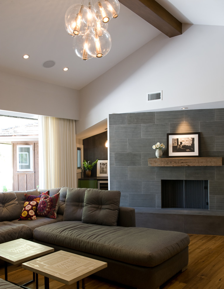 Exemple d'un salon chic de taille moyenne et ouvert avec un mur blanc, un sol en bois brun, une cheminée standard, un manteau de cheminée en pierre et un téléviseur encastré.