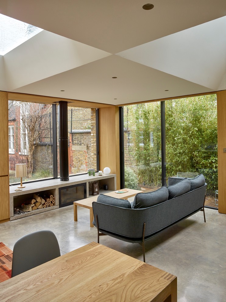Modernes Wohnzimmer mit weißer Wandfarbe, Betonboden, Kaminofen, Kaminumrandung aus Stein und grauem Boden in London