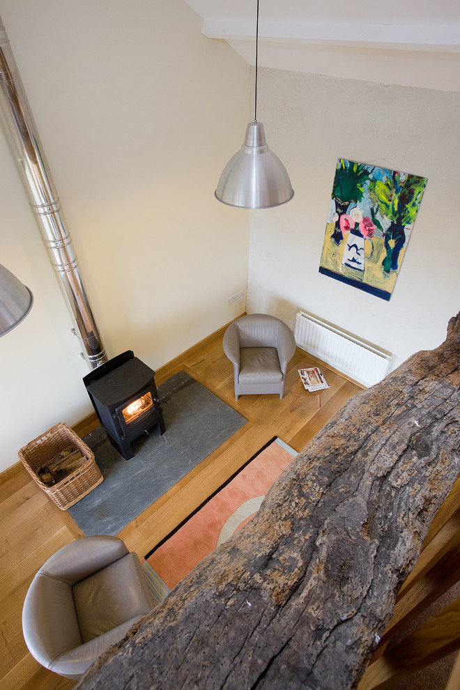 Ejemplo de salón tipo loft tradicional de tamaño medio con paredes blancas, suelo de madera clara, estufa de leña y marco de chimenea de piedra