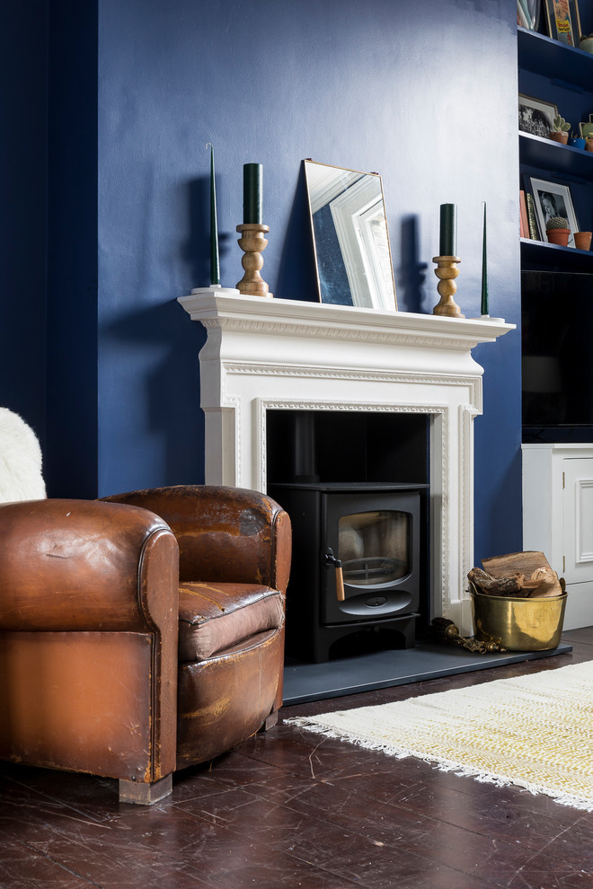ロンドンにあるラグジュアリーな広いトラディショナルスタイルのおしゃれなリビング (青い壁、濃色無垢フローリング、薪ストーブ、漆喰の暖炉まわり、壁掛け型テレビ、茶色い床) の写真