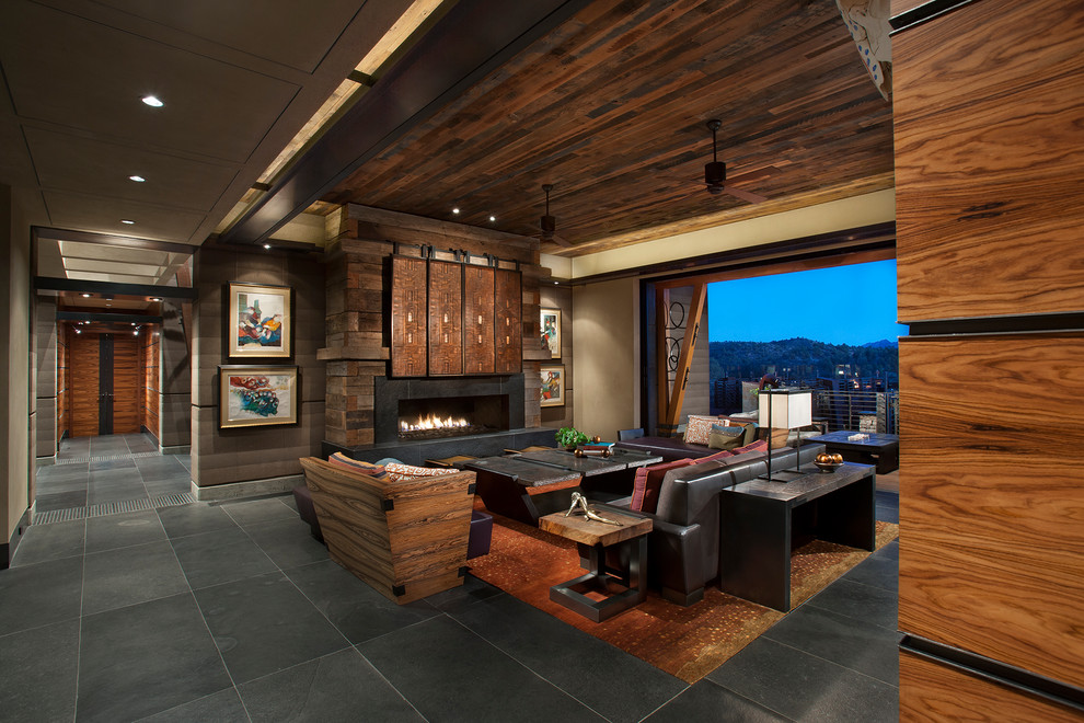 フェニックスにある広いサンタフェスタイルのおしゃれなリビング (茶色い壁、横長型暖炉、石材の暖炉まわり、内蔵型テレビ、黒い床、スレートの床) の写真