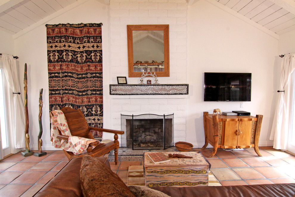 Cette image montre un salon sud-ouest américain avec un mur blanc, tomettes au sol, une cheminée standard et un plafond cathédrale.