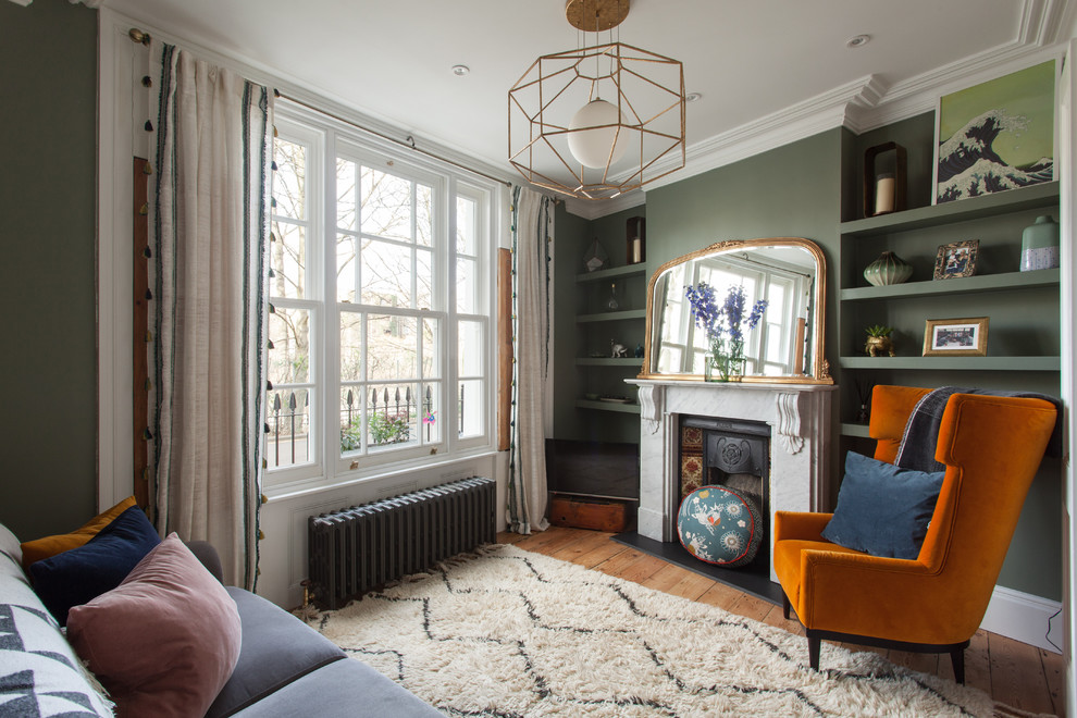 Stilmix Wohnzimmer mit grüner Wandfarbe, braunem Holzboden, Kamin, gefliester Kaminumrandung, freistehendem TV und braunem Boden in London