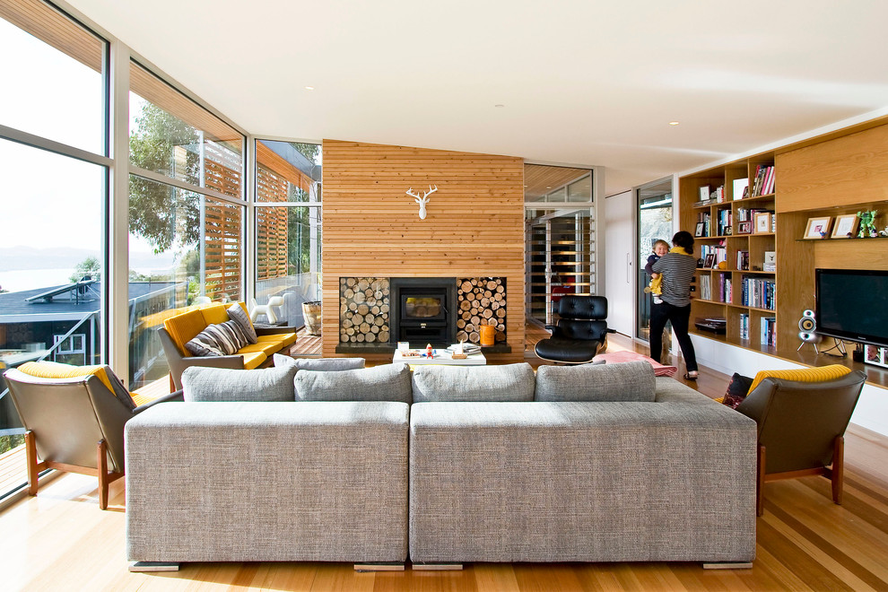 Immagine di un grande soggiorno minimal aperto con libreria, parquet chiaro, camino classico, parete attrezzata e cornice del camino in legno
