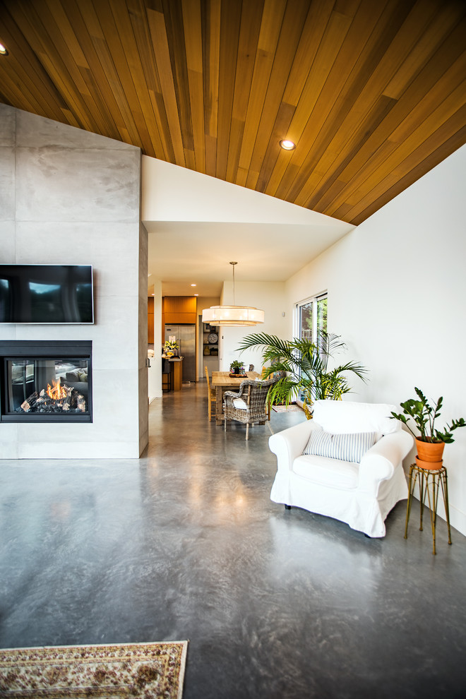 Modelo de salón abierto contemporáneo de tamaño medio con paredes blancas, suelo de cemento, marco de chimenea de hormigón, televisor colgado en la pared y suelo gris