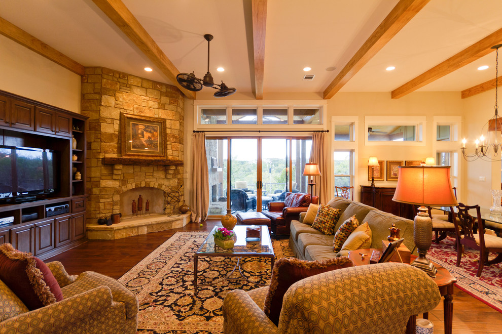 Großes, Offenes Uriges Wohnzimmer mit beiger Wandfarbe, braunem Holzboden, Eckkamin, Kaminumrandung aus Stein, Multimediawand und braunem Boden in Austin