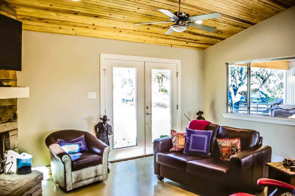Kleines Modernes Wohnzimmer im Loft-Stil mit beiger Wandfarbe, Betonboden, Kamin, Kaminumrandung aus Stein und TV-Wand in Austin