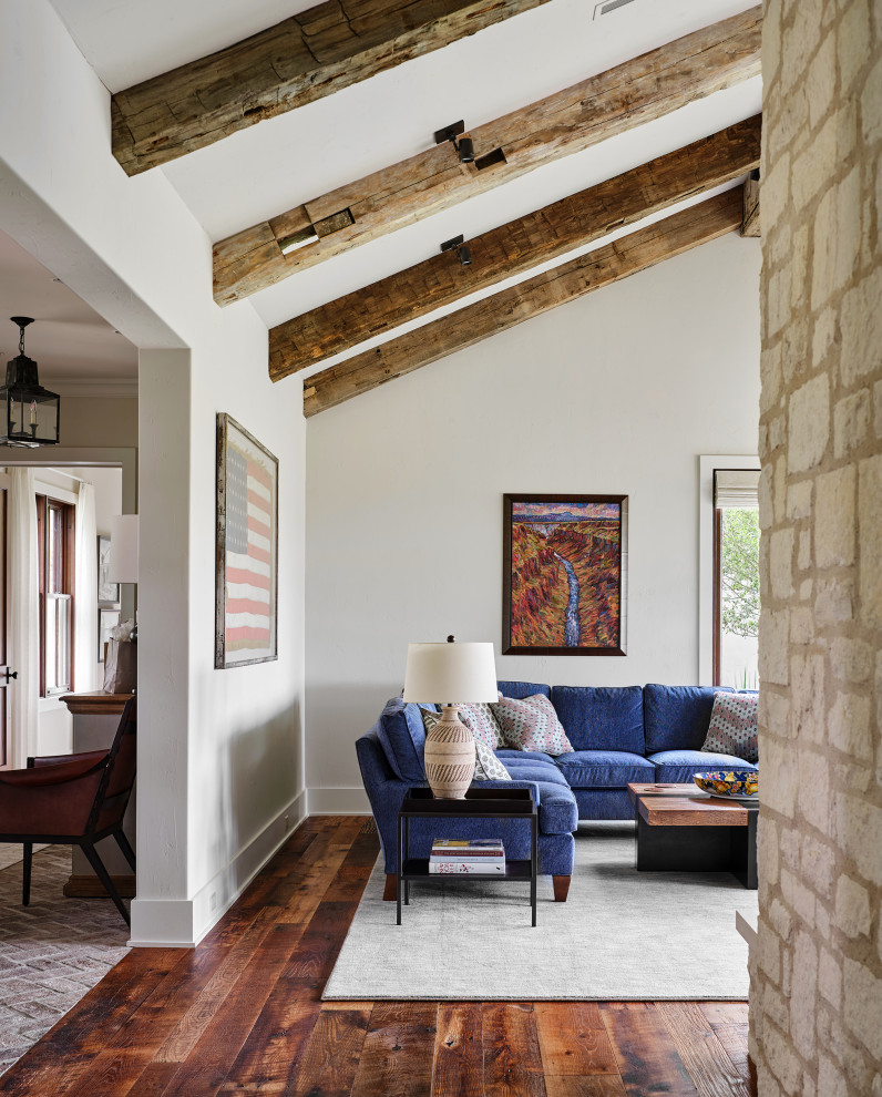 Offenes Landhaus Wohnzimmer mit weißer Wandfarbe, braunem Holzboden, Tunnelkamin, Kaminumrandung aus Stein und freigelegten Dachbalken in Austin
