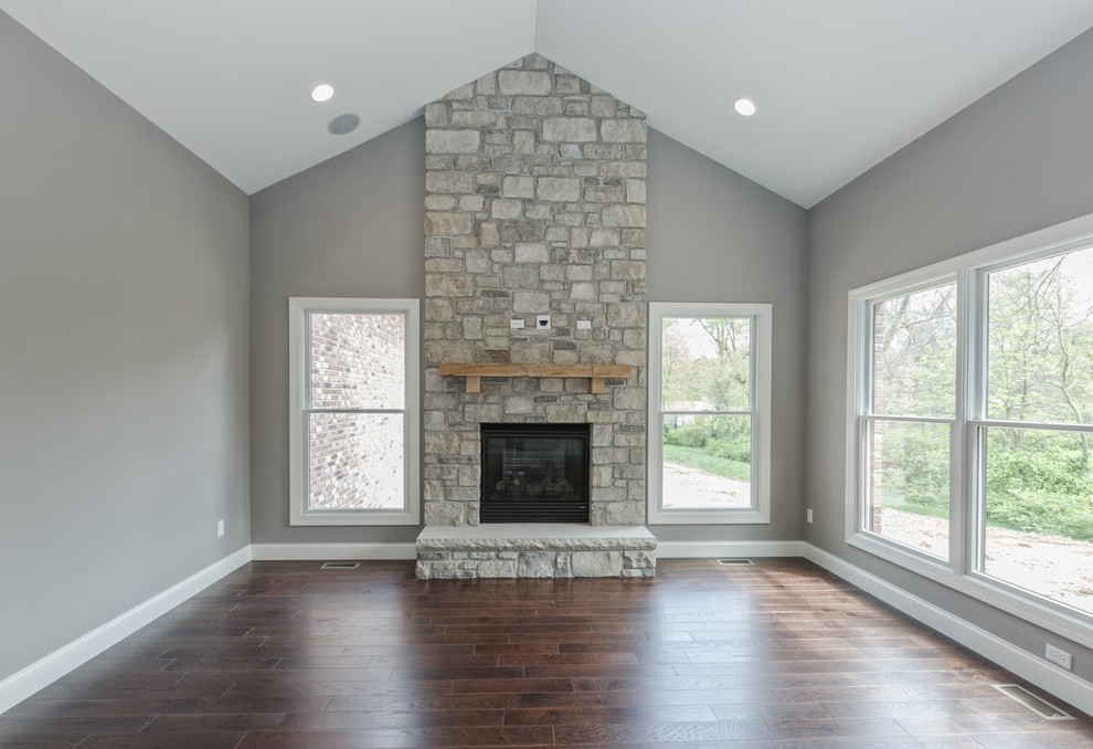 Aménagement d'un grand salon craftsman ouvert avec un mur gris, un sol en bois brun, une cheminée standard, un manteau de cheminée en pierre et un sol marron.