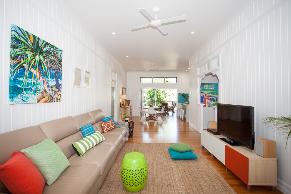 Immagine di un soggiorno tropicale di medie dimensioni e chiuso con pareti bianche, pavimento in legno massello medio e TV autoportante