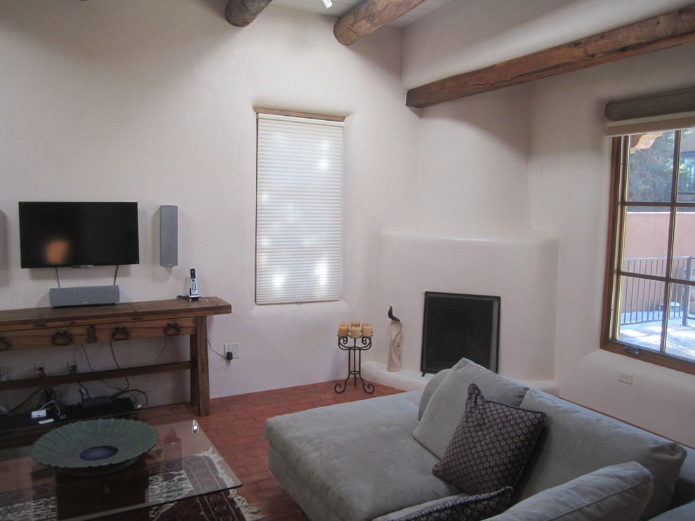 Kleines, Abgetrenntes Mediterranes Wohnzimmer mit beiger Wandfarbe, Backsteinboden, Eckkamin, verputzter Kaminumrandung und TV-Wand in Albuquerque