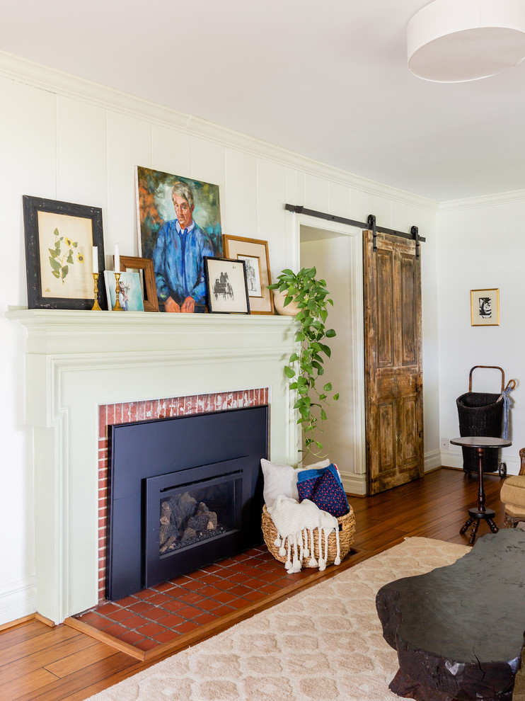 ダラスにある小さなエクレクティックスタイルのおしゃれな独立型リビング (白い壁、無垢フローリング、標準型暖炉、レンガの暖炉まわり、壁掛け型テレビ、茶色い床) の写真