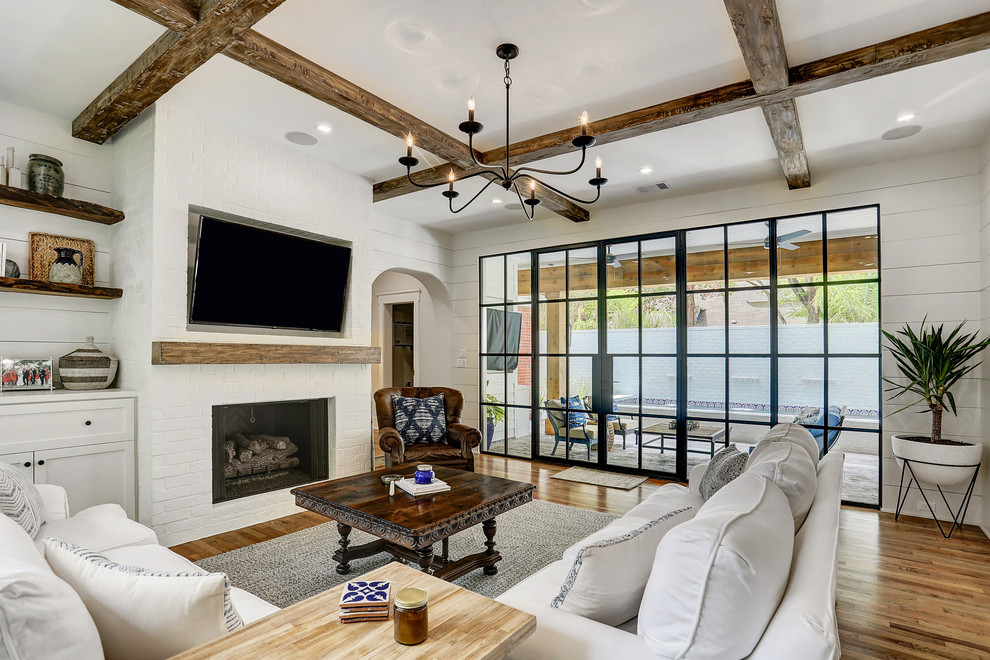 Landhaus Wohnzimmer mit weißer Wandfarbe, braunem Holzboden, Kamin, Kaminumrandung aus Backstein, TV-Wand und braunem Boden in Houston