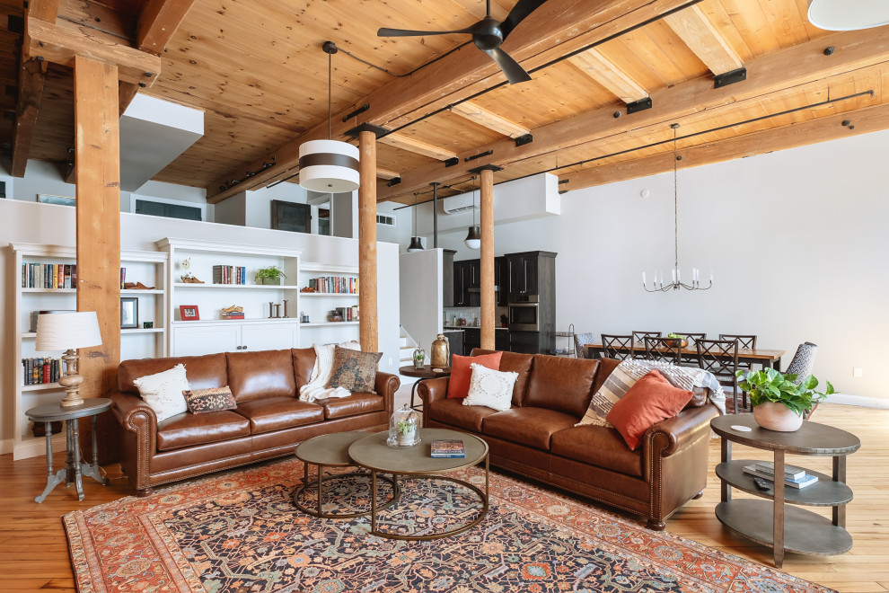 This is an example of an expansive industrial open plan living room in Portland Maine with a reading nook, light hardwood flooring and exposed beams.