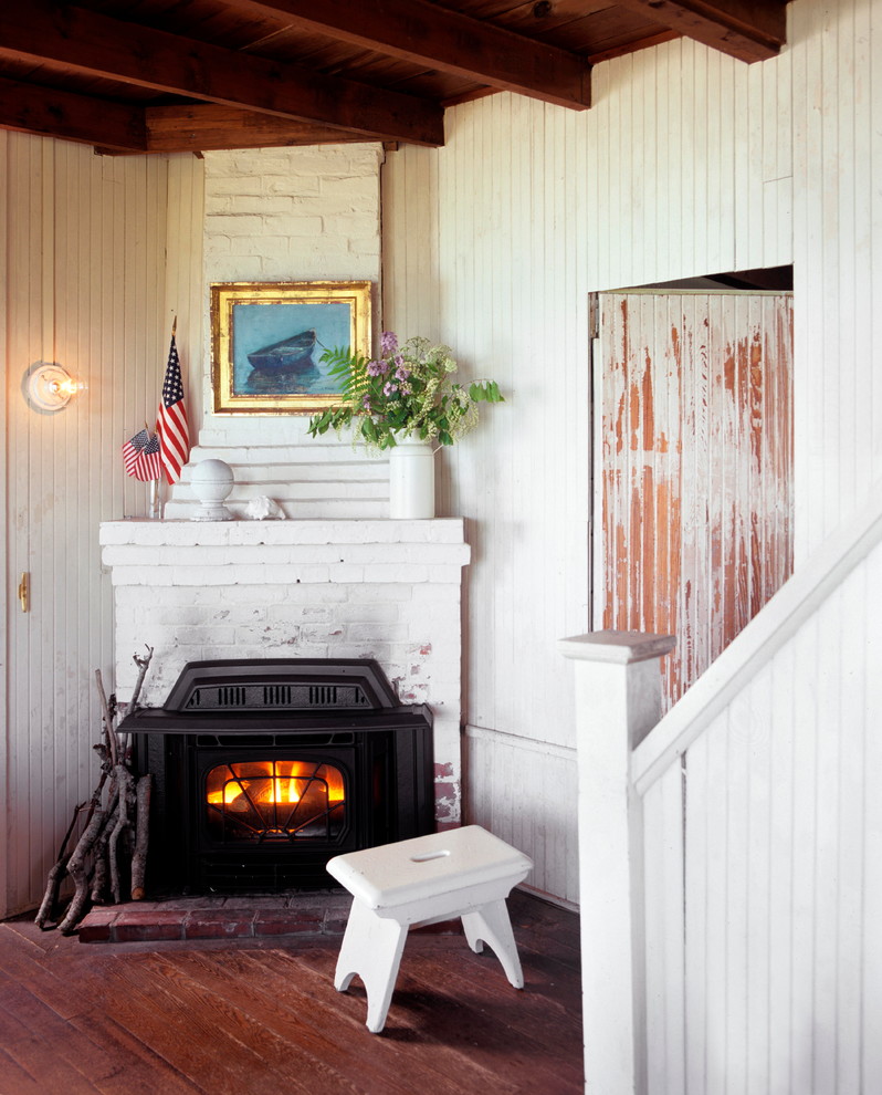 ボストンにあるお手頃価格の小さなビーチスタイルのおしゃれなリビング (白い壁、濃色無垢フローリング、コーナー設置型暖炉、レンガの暖炉まわり、テレビなし) の写真