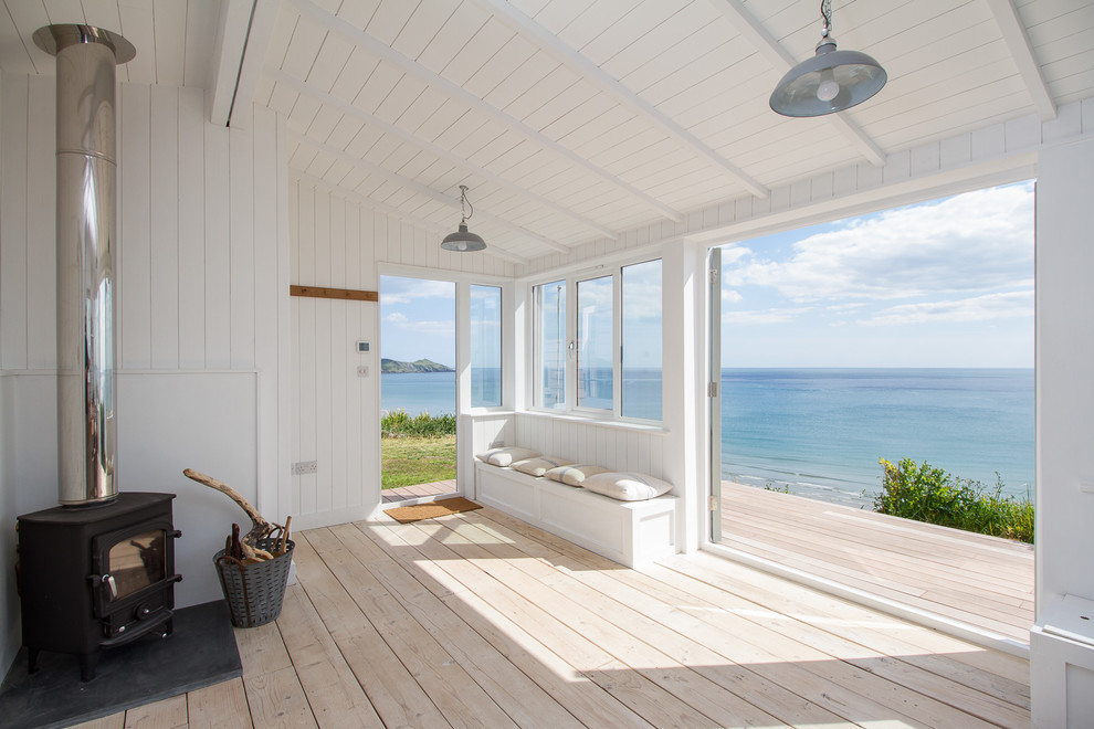Idee per un piccolo soggiorno costiero aperto con pareti bianche, parquet chiaro e stufa a legna