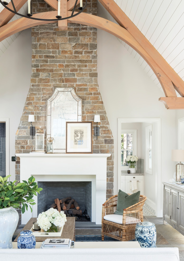 Cette image montre un grand salon traditionnel ouvert avec un mur blanc, un sol en ardoise, une cheminée standard, un manteau de cheminée en pierre, un téléviseur fixé au mur et un sol gris.