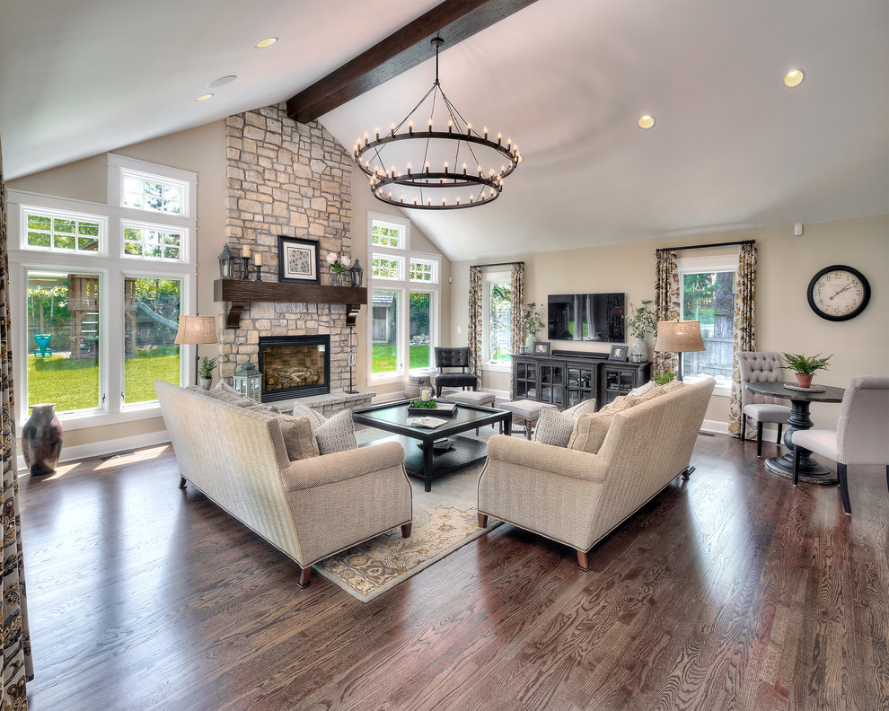 Huge transitional open concept medium tone wood floor living room photo in Kansas City with beige walls, a standard fireplace, a stone fireplace and a wall-mounted tv