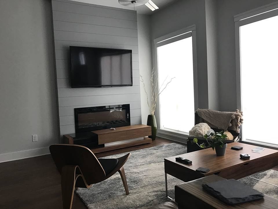 Cette image montre un salon design de taille moyenne et ouvert avec un mur gris, parquet foncé, une cheminée standard, un manteau de cheminée en bois, un téléviseur fixé au mur et un sol marron.