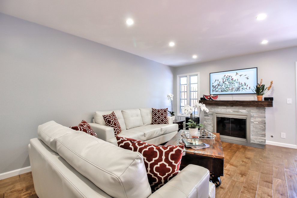 Cette photo montre un grand salon moderne ouvert avec un mur gris, un sol en bois brun, une cheminée standard, un manteau de cheminée en carrelage, un téléviseur fixé au mur et un sol marron.