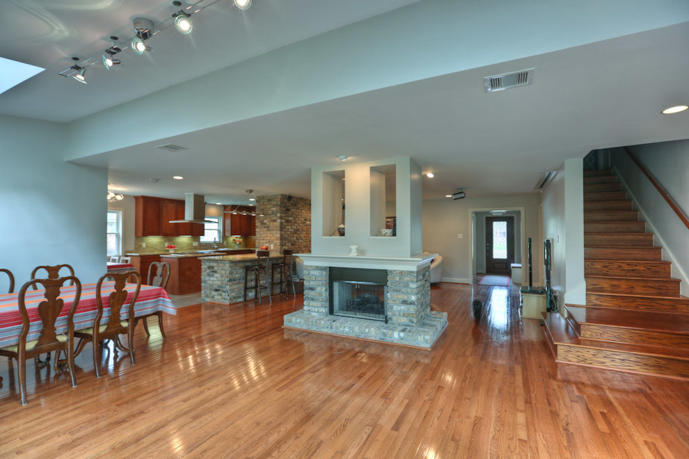 Geräumiges, Offenes Modernes Wohnzimmer mit grauer Wandfarbe, braunem Holzboden, Tunnelkamin und Kaminumrandung aus Backstein in Houston
