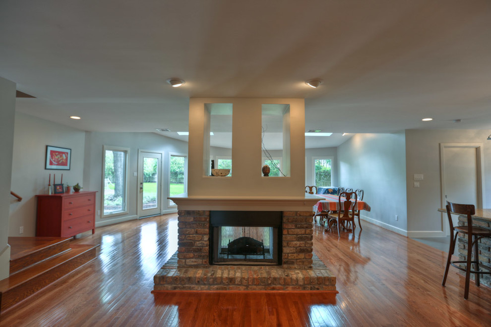 Example of a huge trendy open concept medium tone wood floor living room design in Houston with gray walls, a two-sided fireplace and a brick fireplace
