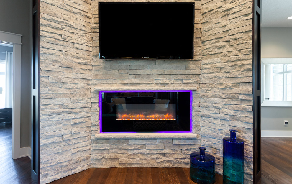 Ejemplo de salón moderno con paredes grises, suelo de madera en tonos medios, chimenea lineal, marco de chimenea de piedra y televisor colgado en la pared