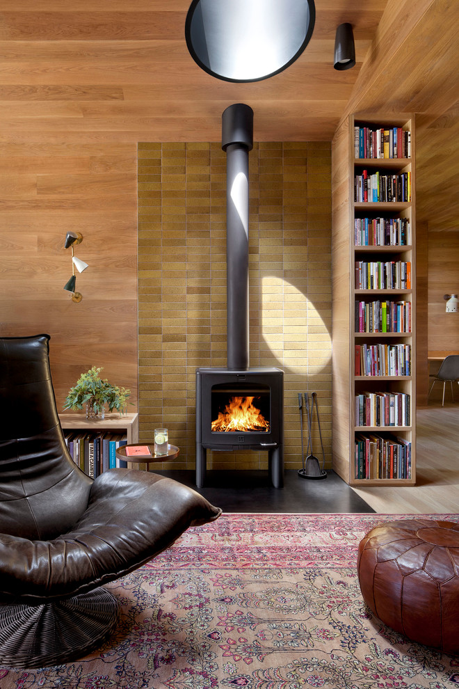 Esempio di un soggiorno design con parquet chiaro, stufa a legna e cornice del camino piastrellata