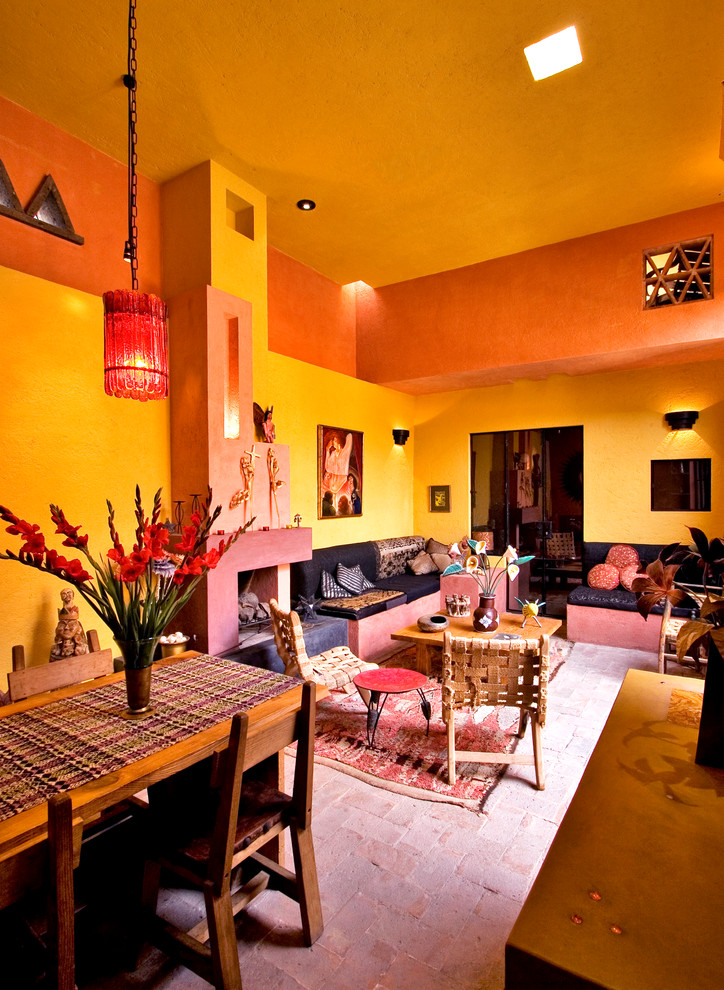 На фото: открытая гостиная комната в стиле фьюжн с желтыми стенами, кирпичным полом, стандартным камином и фасадом камина из штукатурки с