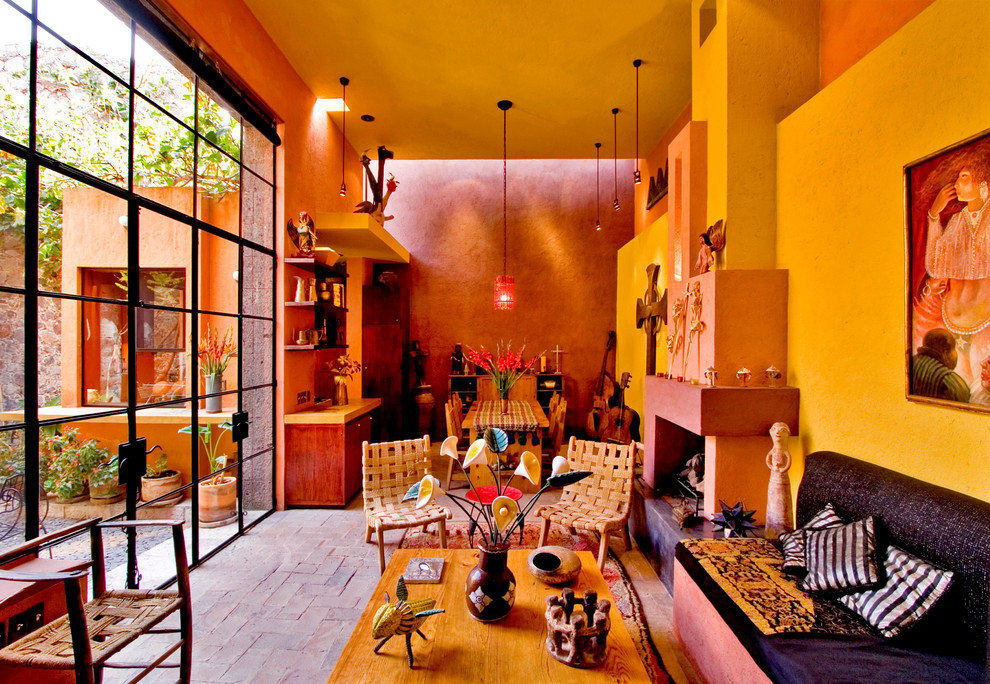 На фото: открытая гостиная комната в стиле фьюжн с разноцветными стенами, стандартным камином, кирпичным полом и фасадом камина из штукатурки