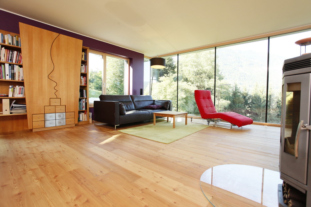 Ejemplo de salón actual de tamaño medio con paredes púrpuras, suelo de madera clara y estufa de leña